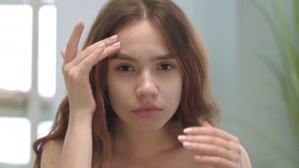 Fiatal nő néz bőr arc tükörben a fürdőszobában. Nő préselő acnes - Felvétel, videó