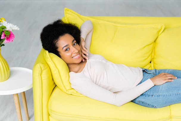 visão de alto ângulo da mulher afro-americana deitada no sofá e olhando para a câmera
 - Foto, Imagem