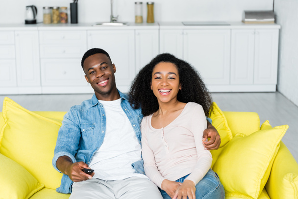 fröhliches afrikanisch-amerikanisches Paar verbringt Zeit zu Hause mit Fernbedienung in der Hand - Foto, Bild