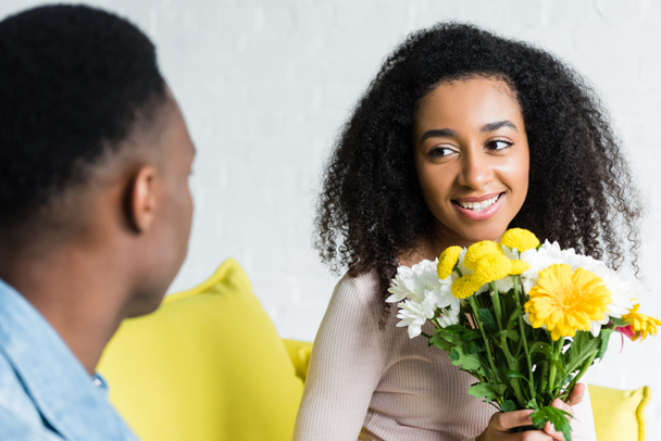 çiçek tutan ve erkek arkadaşı bakarak Afrikalı Amerikalı kadının seçici odak - Fotoğraf, Görsel