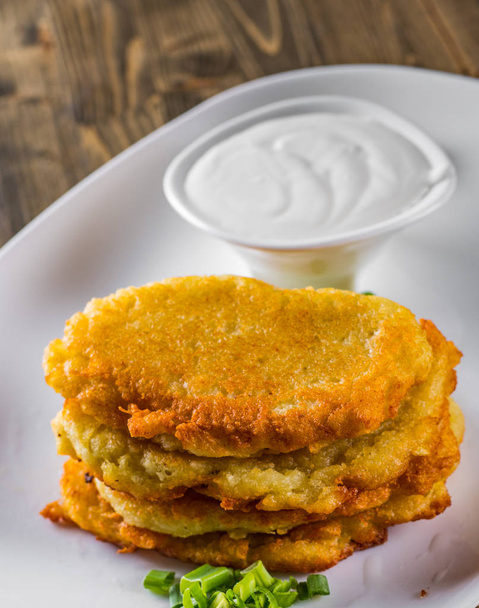 potato pancakes with sour cream in a plate on wooden table - Foto, imagen