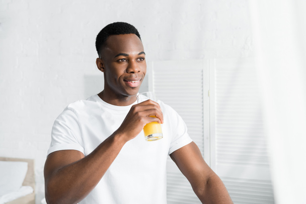 幸せなアフリカ系アメリカ人の男性が目をそらしてオレンジジュースを飲む - 写真・画像