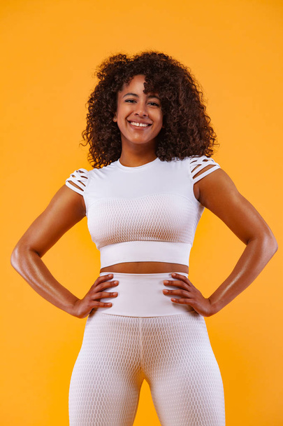 Smiling strong athletic woman with black skin and curly hair, doing exercise on white background wearing sportswear. Fitness and sport motivation. - Photo, image