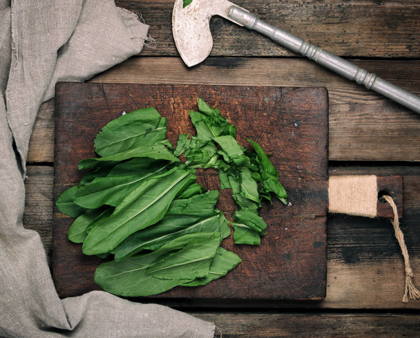 chopped green sorrel leaves on an old brown wooden board - Foto, afbeelding