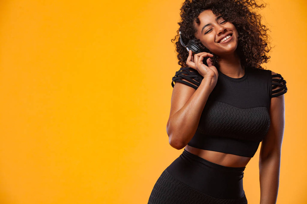 Lifestyle Concept. Portrait of beautiful African American woman with curly hair joyful listening to music on mobile phone. Yellow studio background. Copy Space. - Photo, Image
