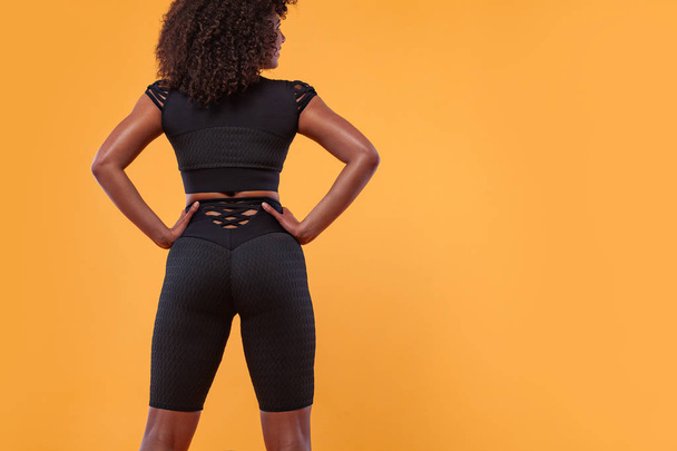 Back of strong athletic woman with black skin and curly hair, doing exercise on white background wearing sportswear. Fitness and sport motivation. - Photo, Image