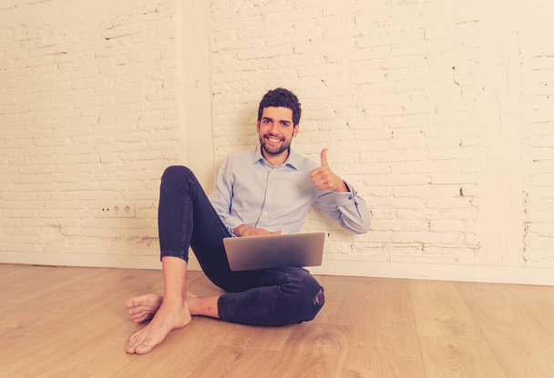 Cheerful young hipster new owner on laptop in his new empty flat happy buying online furniture and appliances getting ready to move in. In successful property home buyer and internet shopping. - Foto, afbeelding