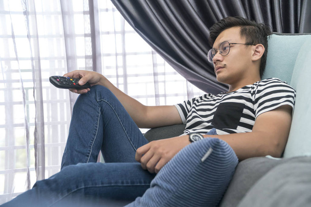 Νεαρός Μαλαισιανός στον καναπέ βλέποντας τηλεόραση χαλαρώνοντας - Φωτογραφία, εικόνα