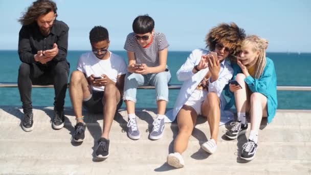 Jovens pessoas diversas com telefones celulares à beira-mar  - Filmagem, Vídeo