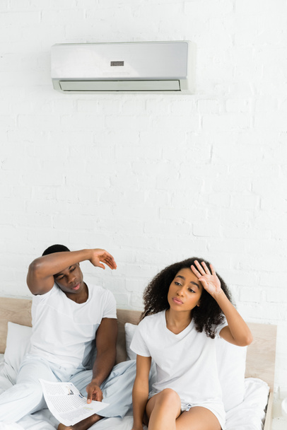 vista de ángulo alto de la pareja afroamericana sentada en la cama en la habitación con aire acondicionado
 - Foto, Imagen