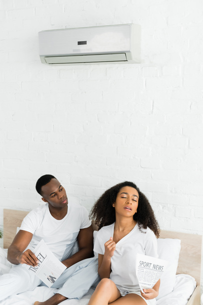 hombre afroamericano mirando a la mujer sudorosa en la habitación con aire acondicionado
 - Foto, Imagen