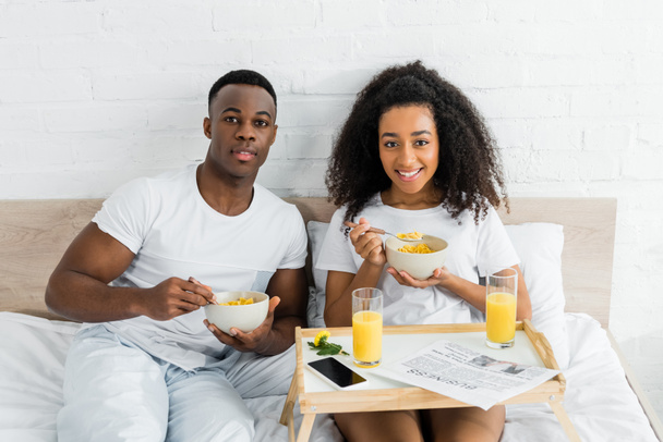 alegre africano americano pareja comiendo desayuno en malo y mirando cámara
 - Foto, imagen