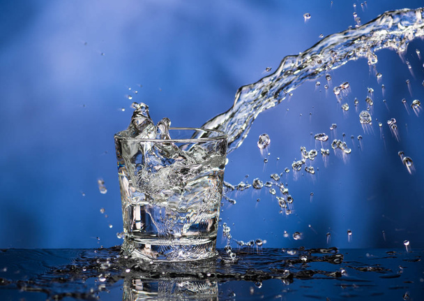 Glass with vodka and a big splash on a colored background - Фото, зображення