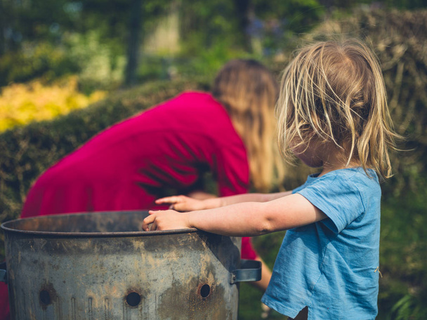 A little toddler is helping his mother put weeds in an incinerator - Fotoğraf, Görsel