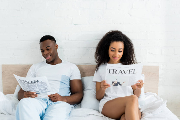 счастливая африканская американская пара читает газеты, лежит в постели
 - Фото, изображение