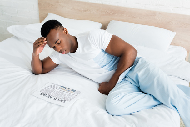 vue en angle élevé d'un homme afro-américain calme lisant un journal, couché sur son lit
 - Photo, image