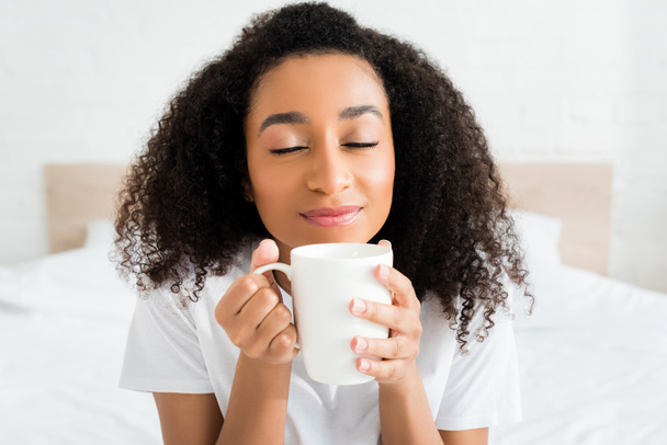 portrait of african american woman closing eyes, holding cup with beverage in hands - Фото, зображення