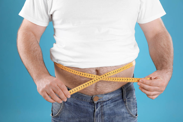Overweight man with large belly and measuring tape on color background, closeup - Foto, imagen