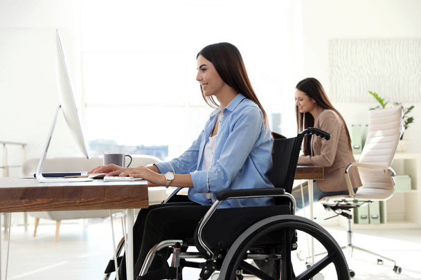 Young woman in wheelchair using computer at workplace - Foto, Imagem