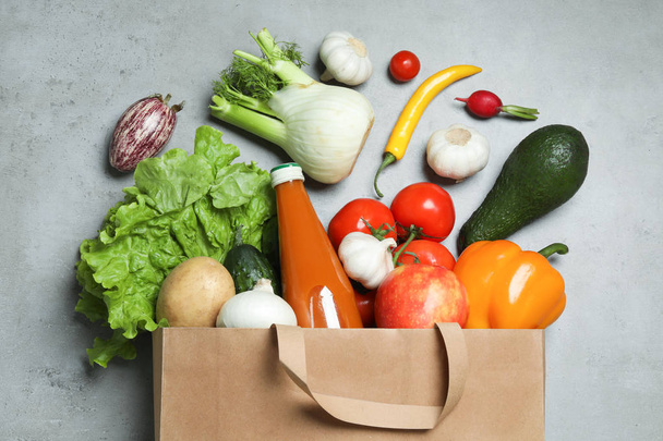 Overturned paper bag with bottle of juice, vegetables and fruits on grey background, flat lay - Foto, afbeelding