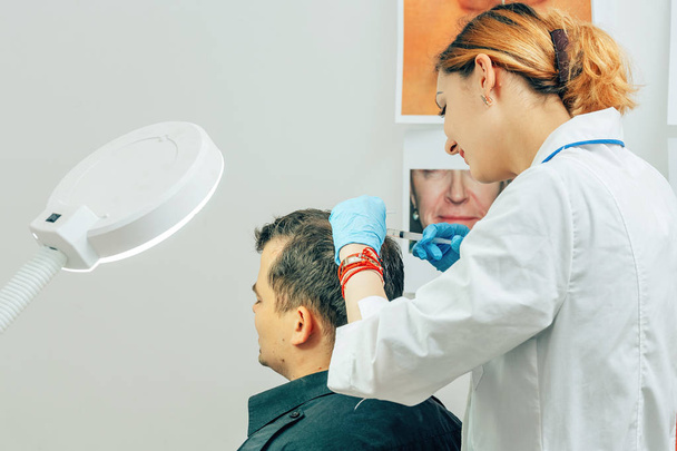 Ένας νέος άντρας με μια φαλάκρα στο γραφείο ενός τρισολόγου αισθητολόγου. Μεσοθεραπεία μαλλιών και κεφαλιού. Καταπολέμηση της απώλειας μαλλιών στους άνδρες. Ενέσεις στο κεφάλι ως μάχη κατά της φαλάκρα στους άνδρες - Φωτογραφία, εικόνα