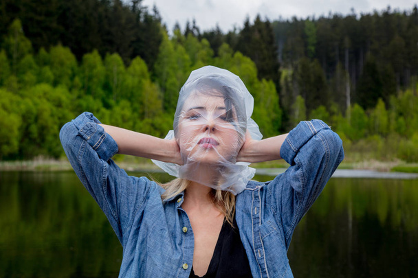 ragazza con sacchetto di cellophane sulla testa vicino al lago e la foresta sullo sfondo
 - Foto, immagini
