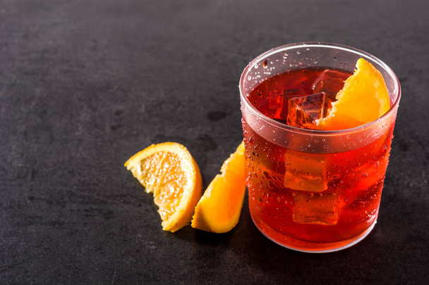 Negroni cocktail with piece of orange in glass on black background. Copyspace - Фото, изображение