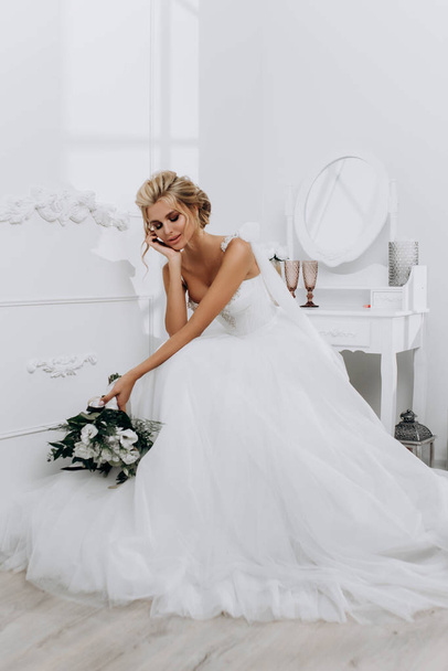 Наречена з красивою зачіскою. Модель блондинки в весільній сукні в білому інтер'єрі
 - Фото, зображення