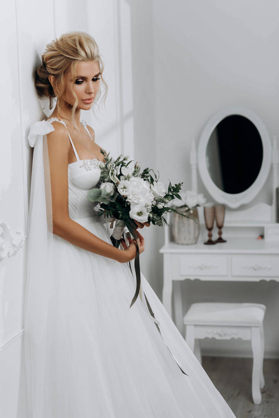 Nevěsta s krásným účesem. Model blondýny ve svatebních šatech v bílém interiéru - Fotografie, Obrázek