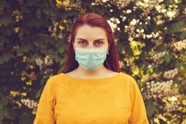 Mala ecología y aire sucio. Una mujer con el pelo rojo y una máscara para protegerse contra infecciones y virus en la calle
. - Foto, Imagen