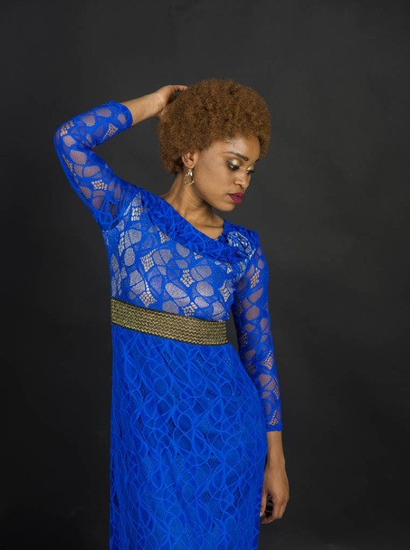 Lady on relaxed face with makeup and afro hairstyle. Lady in dress made out of lace. Woman with african appearance in blue dress looks gorgeous, black background. African females beauty concept - Foto, imagen