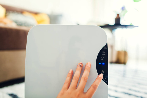 Frau schaltet Luftentfeuchter mit Touchpanel zu Hause ein. modernes Lufttrocknergerät zur Reinigung der Luft - Foto, Bild