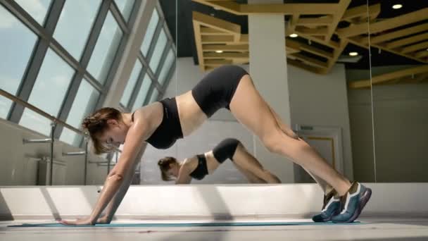 Caucasian brunette in black sportswear doing stretching exercises on the floor. In the background, her reflection in the mirror, a stained glass window and a machine for a ballerina - Кадри, відео