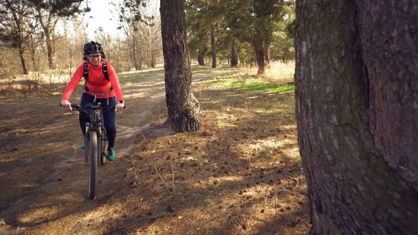 サイクリスト。白人のスポーツウーマンは、春の晴れた日に森のトラックに沿って乗ります。自然の田舎道でマウンテンバイクに乗ってスポーツマンの女の子に乗る。アウトドアスポーツ - 写真・画像