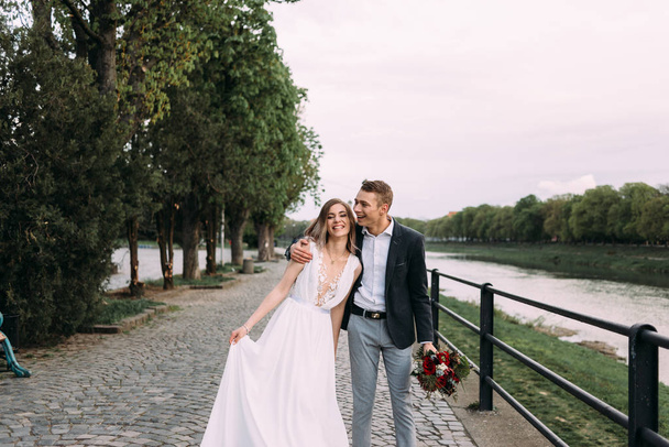 the groom embraces the bride on the river bank. Stylish young and beautiful couple - Photo, Image