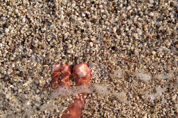 Widok z góry na człowieka stoi boso na plaży. Tekstura DNA, nóg i stóp człowieka utonięcia z zamiatania kolorowych kamieni poniżej na kamienistych kamieniach plaży w morzu z fal i pianki, fale wodne morza. - Zdjęcie, obraz