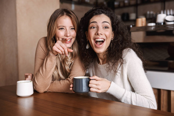 Happy girls friends sitting in cafe talking with each other drinking tea or coffee. - Фото, зображення