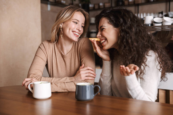 Happy girls friends sitting in cafe talking with each other drinking tea or coffee. - Foto, Imagem