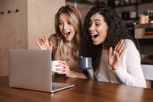 Emotional shocked girls friends sitting in cafe using laptop computer. - Fotografie, Obrázek