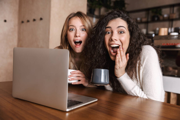 Emotional shocked girls friends sitting in cafe using laptop computer. - Foto, Imagen