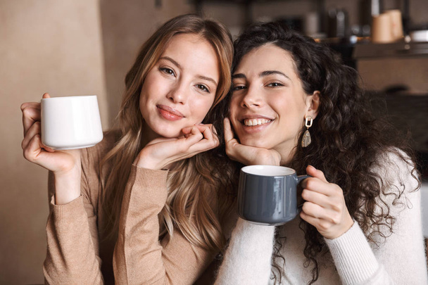 Happy girls friends sitting in cafe talking with each other drinking tea or coffee. - Foto, Imagen