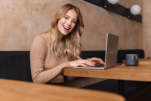 Chica bastante feliz sentado en la cafetería con ordenador portátil
. - Foto, Imagen