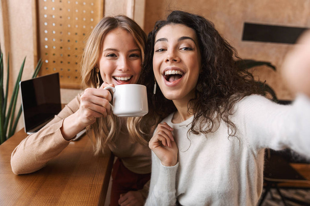 Excited happy pretty girls friends sitting in cafe take a selfie by camera. - Фото, зображення