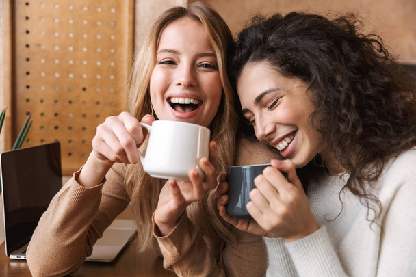 Happy girls friends sitting in cafe talking with each other drinking tea or coffee. - Foto, imagen