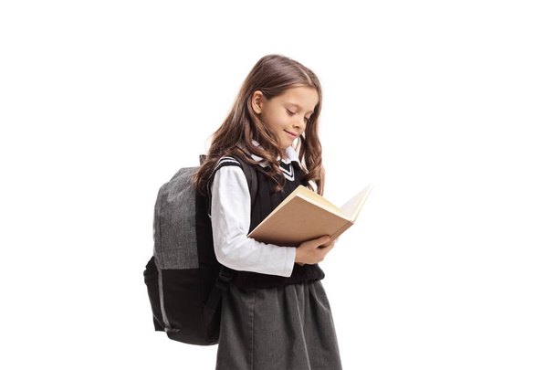 Little schoolgirl in a uniform reading a book isolated on white background - Φωτογραφία, εικόνα