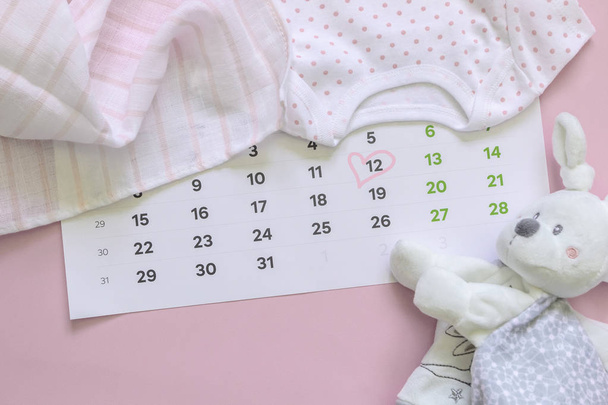 Набір новонароджених аксесуарів в очікуванні дитини - календар з округленим номером 12 (дванадцять), дитячий одяг, іграшки на рожевому тлі. Копіювати простір, плоский простір, вид зверху
. - Фото, зображення
