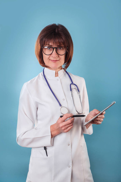 Smiling femal doctor portrait with clipboard on blue background - Zdjęcie, obraz