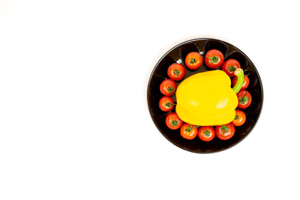 Keltainen paprika tomaatteja musta levy eristetty valkoisella pohjalla. Keltaisten paprikoiden ja punaisten tomaattien koostumus valkoisella taustalla
. - Valokuva, kuva