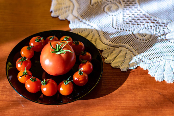 Red tomatoes in a black plate on the kitchen table. - Photo, Image
