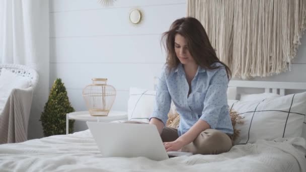 Portrait of an attractive young woman in casual dress at home. young girl working on a laptop while sitting on the bed - Záběry, video